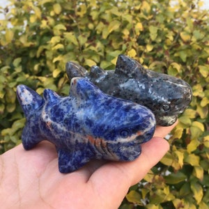 May include: Two carved shark figurines, one blue and one gray, made of polished stone. The blue shark has a white stripe down its side.