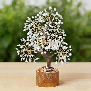 May include: A decorative tree sculpture with a brown trunk and branches made of gold-colored wire. The tree's leaves are small, light blue and white stones. The tree sits in a wooden pot filled with colorful stones.