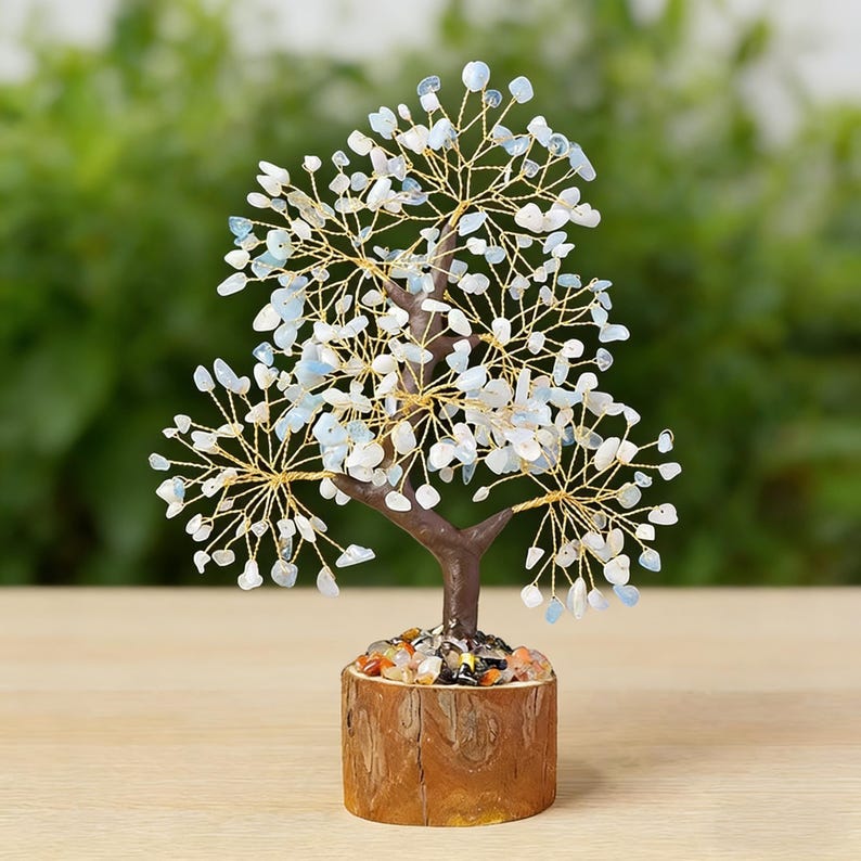 May include: A decorative tree sculpture with a brown trunk and branches made of gold-colored wire. The tree's leaves are small, light blue and white stones. The tree sits in a wooden pot filled with colorful stones.