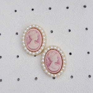 Pu&ograve; includere: Un paio di orecchini con cammeo rosa con bordo dorato e bordo di perle.