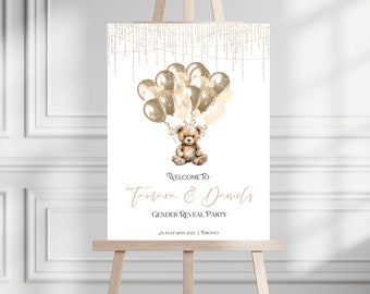 May include: A white welcome sign with gold glitter accents and a teddy bear holding balloons. The sign reads "Welcome to [Name] & [Name]'s Gender Reveal Party" with the date and location below.