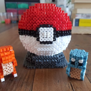 Pokebola hecha de cuentas de hierro en un soporte con charmander y squirtle