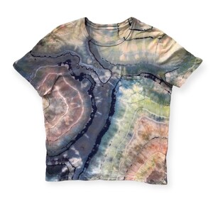 Pode incluir: Uma camiseta de manga curta com estampa tie-dye e um bolso do lado esquerdo. A camiseta apresenta um padrão de redemoinho em cores azul, verde e marrom.