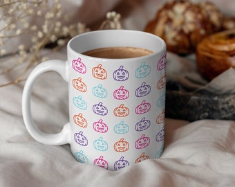 May include: White ceramic mug with a pattern of colorful outlined jack-o'-lantern faces. The mug is filled with a brown liquid.