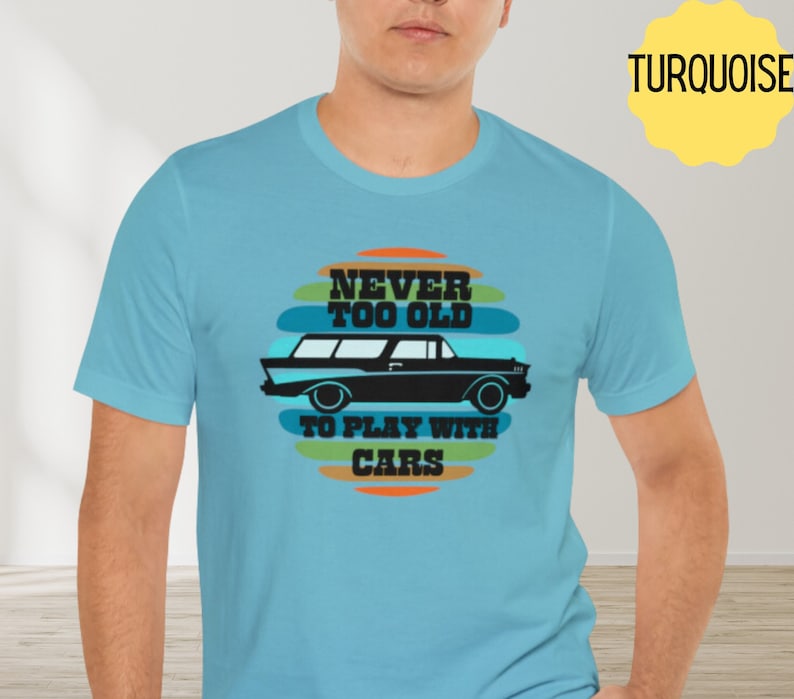 Puede incluir: Una camiseta azul turquesa con un gr&aacute;fico retro de un coche y el texto "Never Too Old To Play With Cars".
