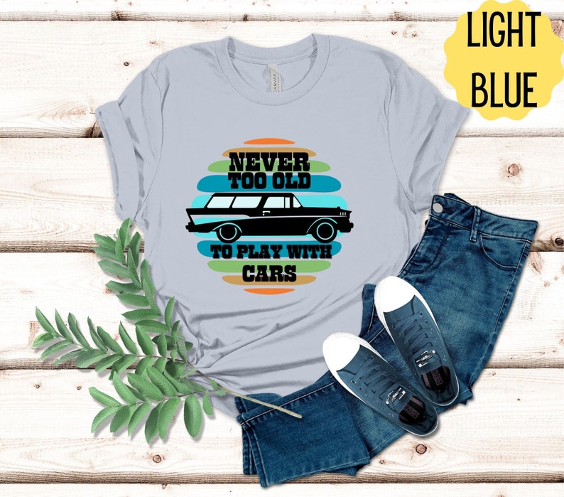 Puede incluir: Camiseta azul claro con un gr&aacute;fico de coche vintage y el texto "Never too old to play with cars".