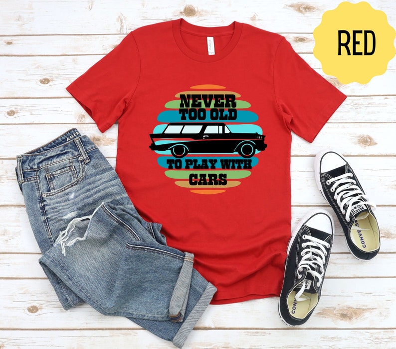 Puede incluir: Camiseta roja con un gr&aacute;fico de coche vintage y el texto "Never Too Old To Play With Cars".