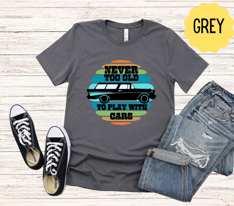 Puede incluir: Una camiseta gris con un gr&aacute;fico de coche vintage y el texto "Never Too Old To Play With Cars".