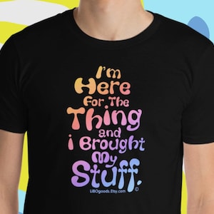May include: Black t-shirt with a rainbow gradient design that says "I'm Here For The Thing And I Brought My Stuff."  The text is in a playful, rounded font.