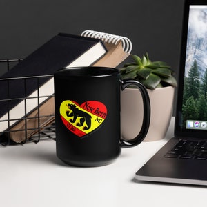 May include: Black ceramic mug with a white heart design featuring a black bear, the text "New Bern NC 1710" and the words "City of the Bear, Founded 1710".