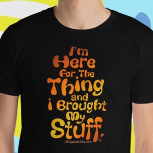 May include: Black t-shirt with orange and yellow text that reads "I'm Here For The Thing and I Brought My Stuff."  The text is in a fun, bubbly font.  The text also includes the website "LibOgoods.Etsy.com".