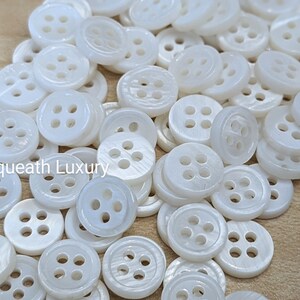 May include: A pile of white, round, four-hole shell buttons.