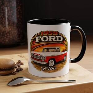 May include: A white ceramic mug with a black interior and handle, featuring a graphic illustration of a red and white 1959 Ford F-100 pickup truck. The design includes the text 1959 FORD and F-100 set against a sunset-colored circular background.