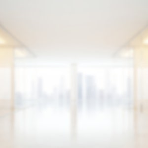 Puede incluir: Imagen borrosa de un interior de oficina moderno. El espacio presenta un diseño brillante y abierto con paredes de vidrio y una vista de un paisaje urbano en la distancia. La paleta de colores es principalmente blanca y beige, creando un ambiente limpio y aireado.