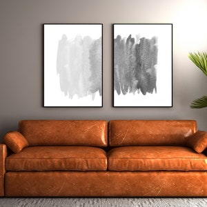 Puede incluir: Un sofá de cuero marrón con dos pinturas abstractas en blanco y negro colgadas encima. Un palmera en maceta está a la derecha del sofá.