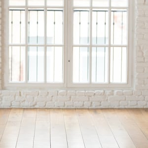 May include: A white brick wall with two large windows and a wooden floor. The windows have white frames and black metal bars.