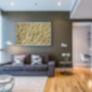 Pode incluir: Uma sala de estar com um sofá cinza, uma mesa de centro e uma imagem emoldurada na parede. A sala tem piso de madeira e uma porta que leva a outra sala.