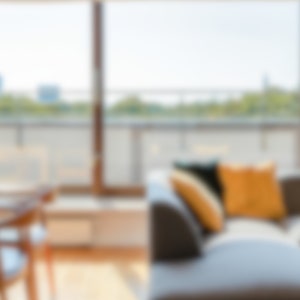 Könnte beinhalten: Ein modernes Wohnzimmer mit einem dunkelgrauen Ecksofa. Das Sofa ist mit dekorativen Kissen in Gelb- und Dunkelgrüntönen ausgestattet. Ein großes Fenster bietet einen Blick ins Freie, mit einem Holztisch und Stühlen im Vordergrund.