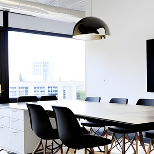 May include: A modern conference room with a large window, a long wooden table, and black chairs. A black television is mounted on the wall. A silver dome-shaped light fixture hangs from the ceiling.