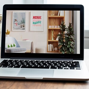 May include: A laptop computer displaying a mock-up of a living room interior design with two framed prints on the wall. One print features a snowman in a winter scene, and the other print says "Merry Merry Merry Christmas".