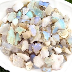 May include: A bowl filled with a variety of small, rough, white, blue, and green opal gemstones. The opal pieces are irregular in shape and size.