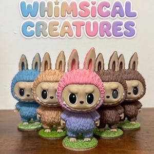 May include: A collection of six whimsical creature figurines. Each figure has a furry body and a head with large eyes and pointed ears. The figurines are in various colors, including blue, brown, and pink, and stand on small green bases. The text "WHIMSICAL CREATURES" is above the figurines.