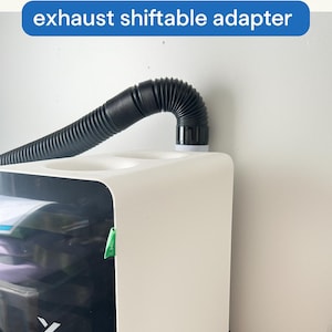 May include: White xTool AP2 Filter System with a black flexible exhaust hose. The text "xTool AP2 Filter System" and "exhaust shiftable adapter" are visible. The unit is on a wooden surface.