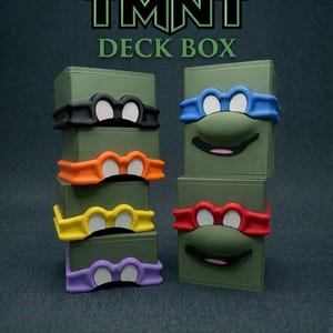 May include: Green deck boxes featuring Teenage Mutant Ninja Turtle character designs. Each box has a different colored mask and facial features. The TMNT logo and "Deck Box" text are at the top.