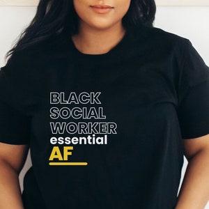 May include: Black t-shirt with the text "BLACK SOCIAL WORKER essential AF" in white and yellow lettering.