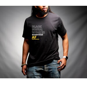 May include: A black t-shirt with white text that reads "Black Social Worker Essential AF" in a stacked format. The text is outlined in black.