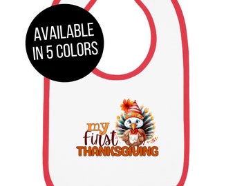 Puede incluir: Un babero blanco para bebé con ribete rojo. El babero tiene un lindo pavo de dibujos animados con un sombrero de peregrino y el texto "my first thanksgiving".
