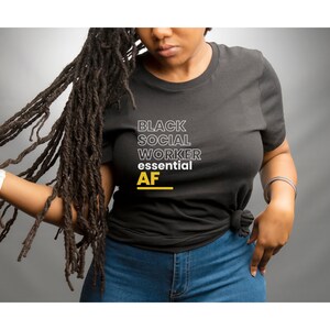 May include: A black t-shirt with the text "Black Social Worker essential AF" in white and yellow lettering.