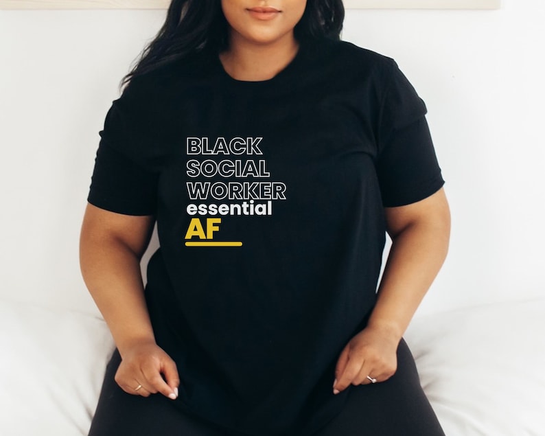 May include: Black t-shirt with the text "BLACK SOCIAL WORKER essential AF" in white and yellow lettering.