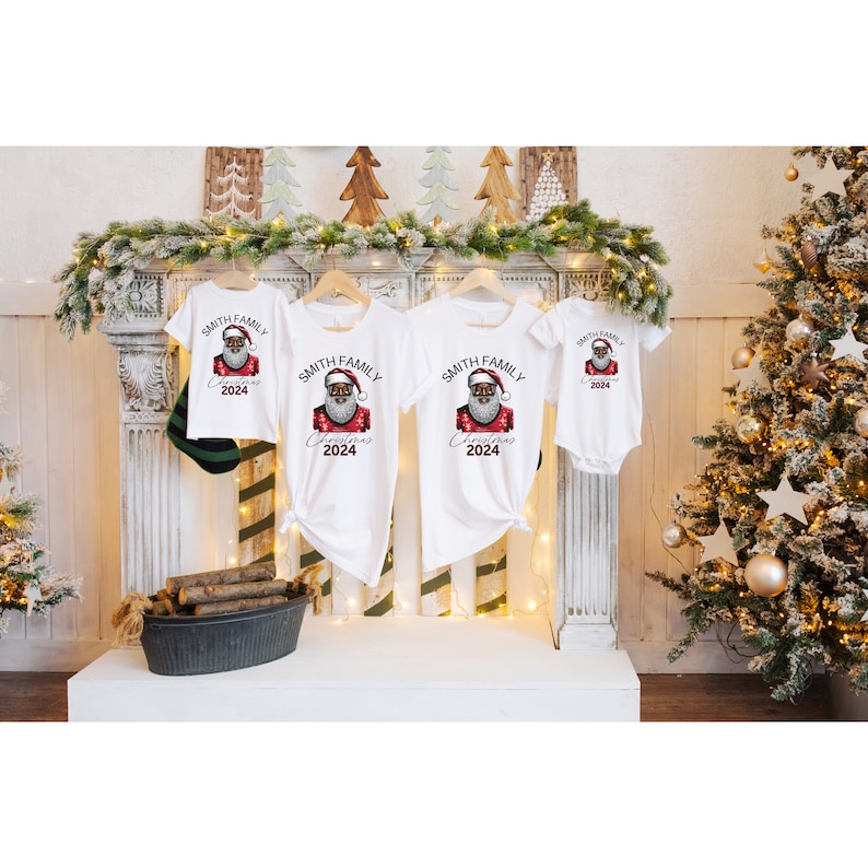 May include: Four white t-shirts featuring a black Santa Claus graphic and the text "Smith Family Christmas 2024". The shirts are displayed on a white shelf in front of a fireplace and Christmas trees.