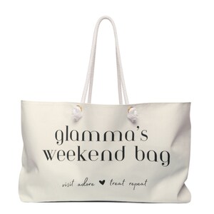 May include: White canvas tote bag with black text that reads "glamama's weekend bag" and "visit adore &hearts; treat repeat".
