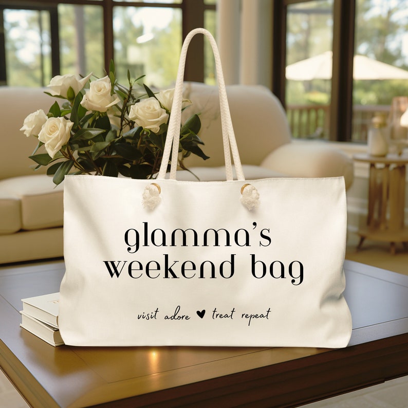 May include: White canvas tote bag with black text that reads "glamama's weekend bag" and "visit adore treat repeat" with a heart symbol between the words "adore" and "treat".