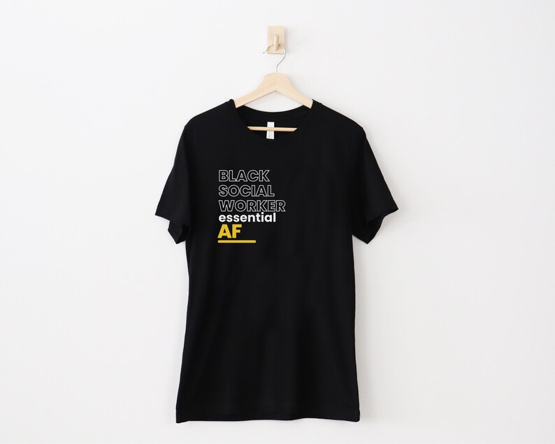 May include: Black t-shirt with white text that reads "Black Social Worker Essential AF" in a bold, outlined font. The word "AF" is in yellow.