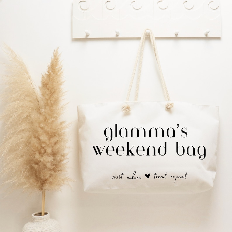 May include: White canvas tote bag with black text that reads "glamama's weekend bag" and "visit adore treat repeat".