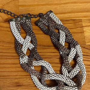Puede incluir: Un collar de cadena trenzada blanco y marrón con un cierre de metal.