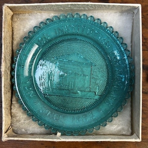 May include: A teal-colored glass plate with a scalloped edge, presented in a box. The plate features an embossed building design and the text "NEW BEDFORD INSTITUTION FOR SAVINGS SINCE 1825".