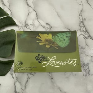May include: A package of green stationery envelopes from The Alive Collection, labeled "Lovenotes." The design features a yellow flower and a green butterfly. The package is green with white text and a price tag.