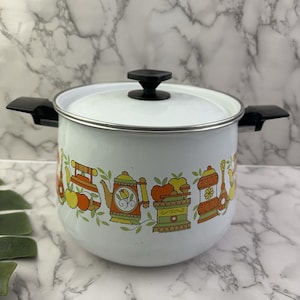 May include: White enamel pot with a black lid and handles. The pot features a decorative band of orange, yellow, and green kitchen-themed illustrations. The pot is designed for cooking and has a silver rim.