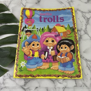 Puede incluir: Un libro infantil vintage "Norfin Trolls" con un borde amarillo. La portada presenta tres personajes de trolls con pelo colorido, que llevan mochilas y sostienen libros. El fondo incluye una casa, un columpio y un globo aerostático.