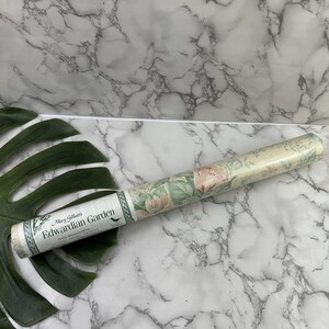 Puede incluir: Rollo de papel pintado con un diseño floral de flores rosas y verdes sobre un fondo crema. La etiqueta dice "Mary Gilliat's Edwardian Garden". El papel pintado es de vinilo y tiene un borde decorativo.