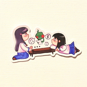 May include: A sticker depicting two anime-style girls in school uniforms, one seated and one reclining at a dark brown table. A green spirit holds a paper with musical notes. Speech bubbles and musical notes are also present.