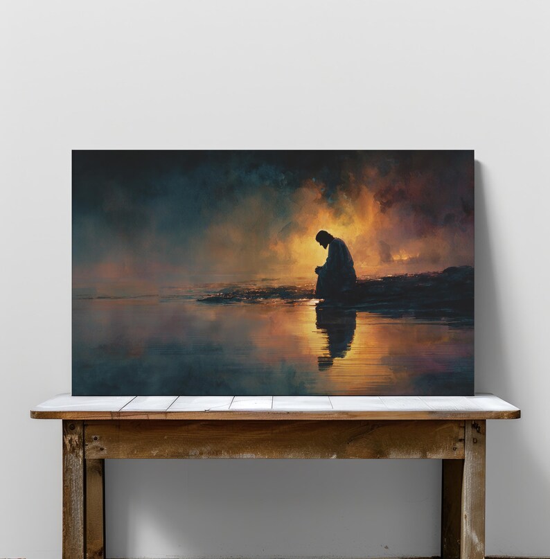 May include: A canvas print showing a silhouetted figure seated by water, with a reflective surface. The artwork uses a warm palette of oranges, yellows, and blues, creating a calm atmosphere. The print is displayed on a wooden table, adding to the overall aesthetic.