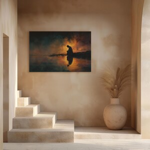 May include: A framed art print showing a silhouetted figure kneeling by water, with a fiery sunset reflected. The artwork hangs on a beige wall, with a staircase and decorative vase in the foreground, creating a serene atmosphere.