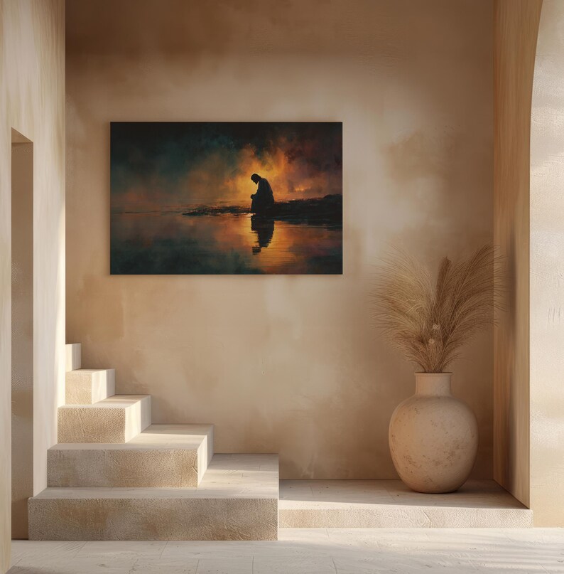 May include: A framed art print showing a silhouetted figure kneeling by water, with a fiery sunset reflected. The artwork hangs on a beige wall, with a staircase and decorative vase in the foreground, creating a serene atmosphere.