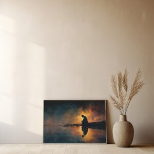 May include: A framed art print showing a silhouetted figure by water, with a sunset reflected in the water. The artwork uses orange, blue, and yellow, creating a calm and reflective scene. The print is displayed on a wall.