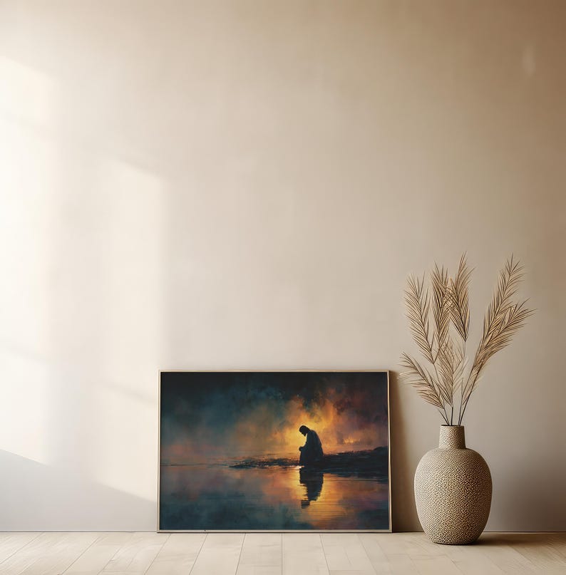 May include: A framed art print showing a silhouetted figure by water, with a sunset reflected in the water. The artwork uses orange, blue, and yellow, creating a calm and reflective scene. The print is displayed on a wall.